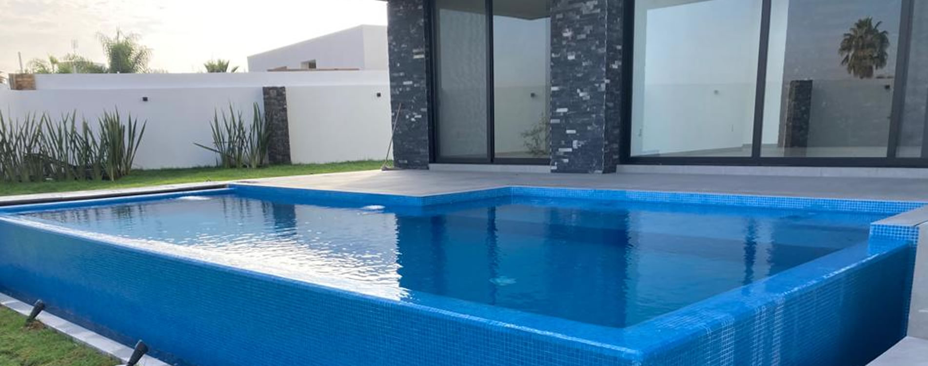 Alberca con azulejos azules y agua clara, ubicada en un entorno residencial moderno.